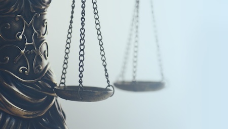 Close-up of scales of justice statue with blurred courthouse background.